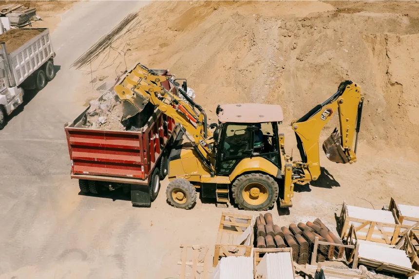 CAT 428 backhoe loader tipping rubble from its front bucket into the bed of a red truck