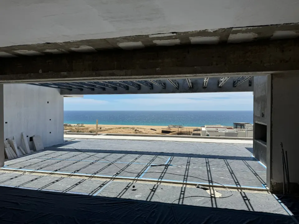 View from inside a concrete house structure under construction, where the open frame looks out over a terrace, the sea and the far shore