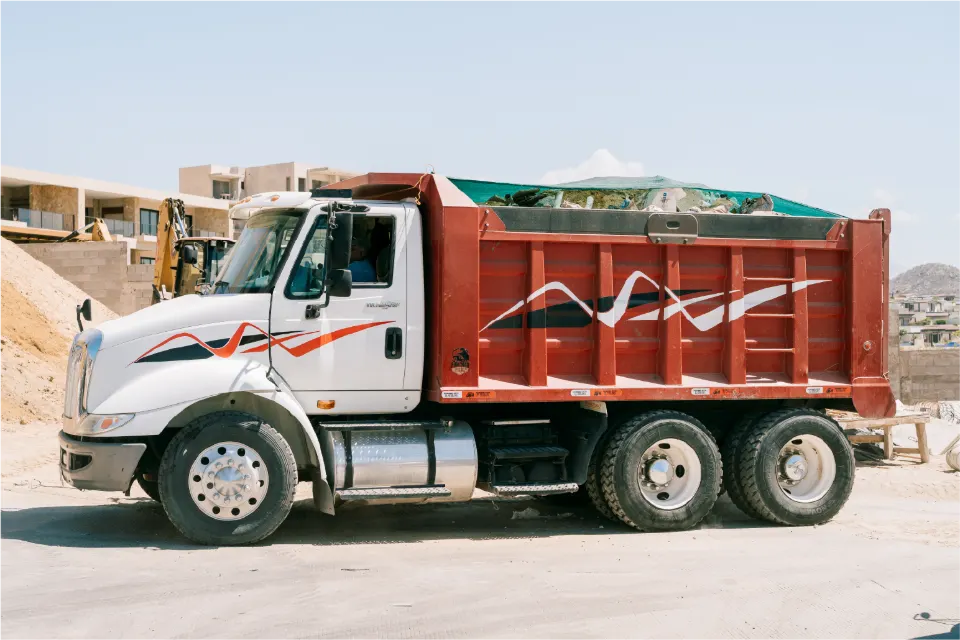 Side view of the white International TranStar, red body loaded and covered, with swooping stripe graphics, parked on a paved site road