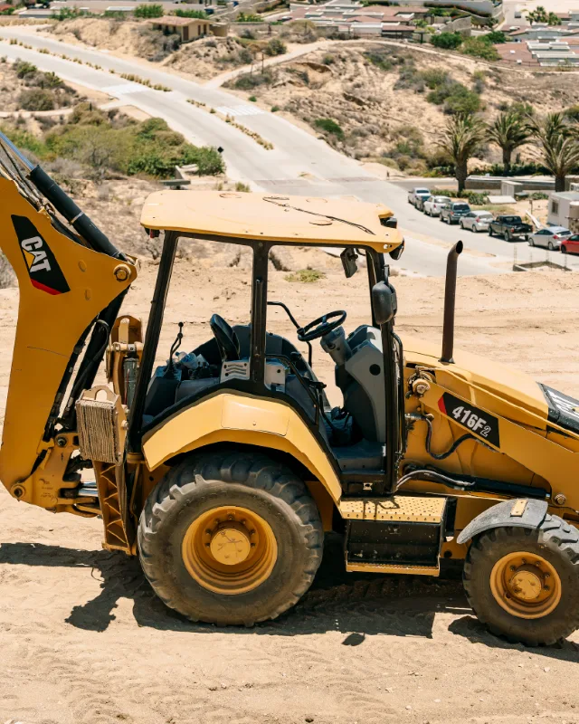 CAT backhoe loader working on a hillside lot above a Los Cabos neighborhood