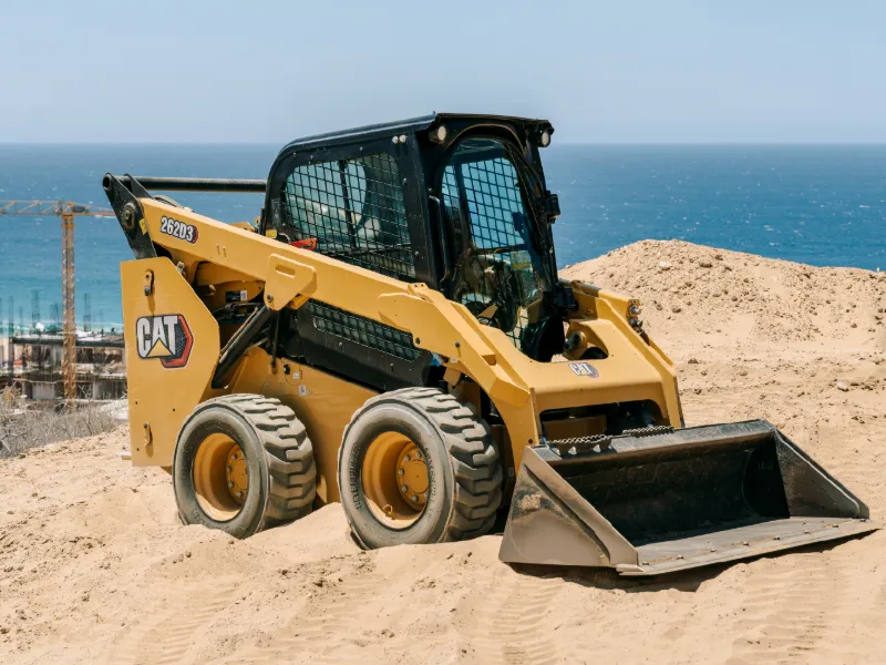 CAT skid steer loader on a sandy lot above the ocean