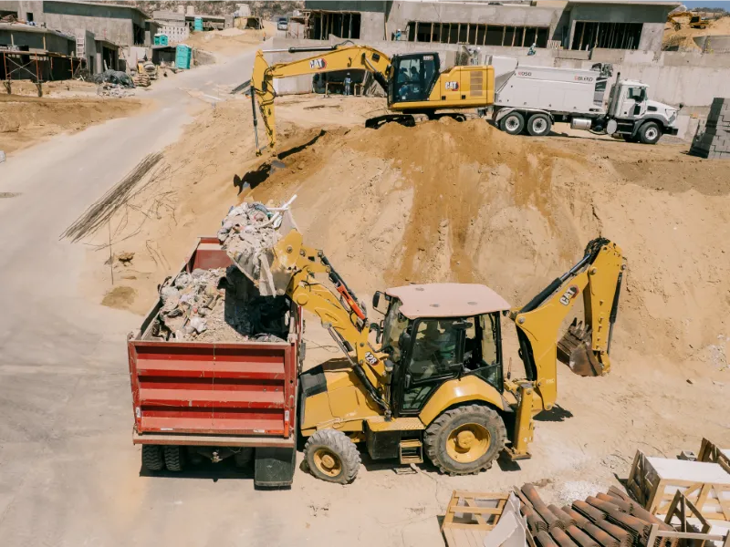 CAT backhoe loader loading debris into a red dump truck on a residential site