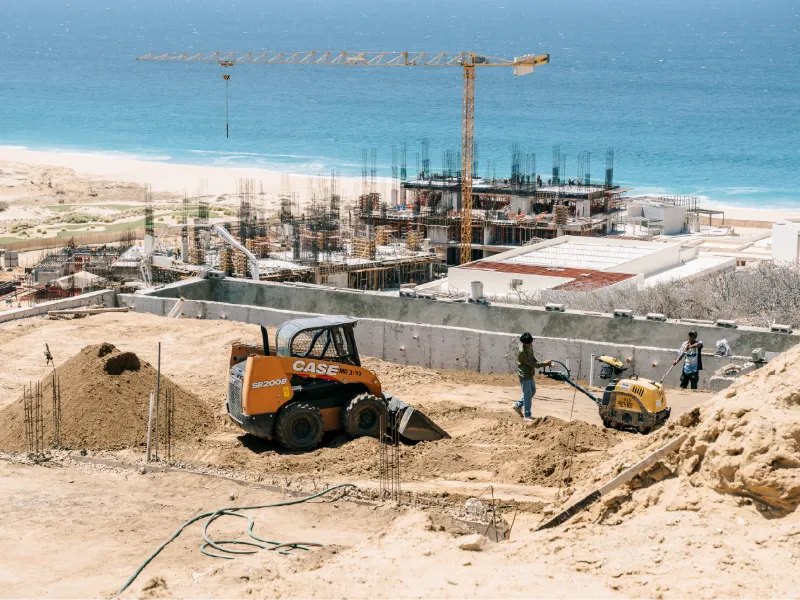 Skid steer and crew working on a beachfront construction site with a tower crane