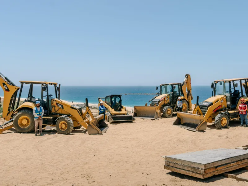 CAT backhoe loaders from the Creatio rental fleet parked above the beach in Los Cabos