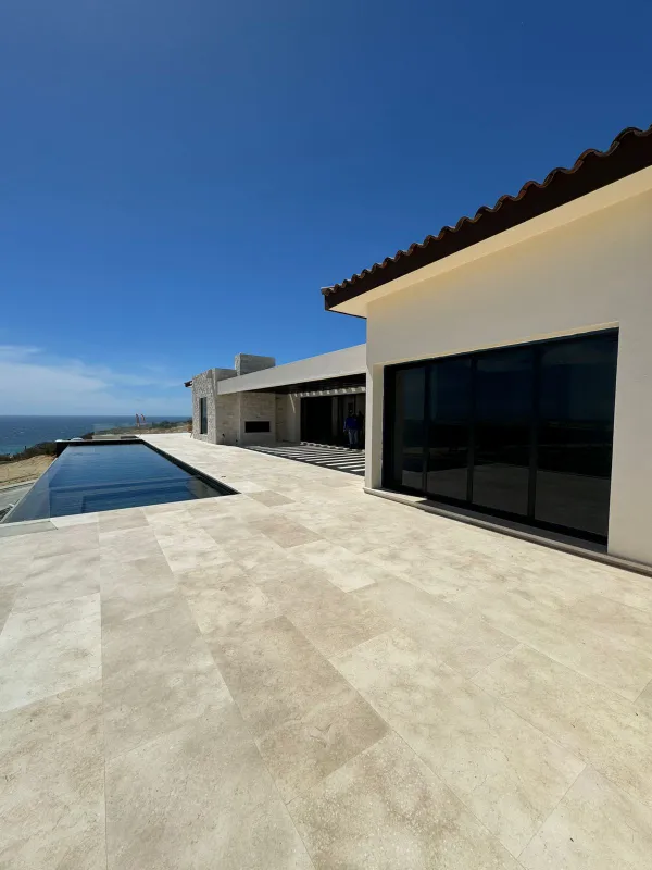 White modern home with a tiled roof, a stone deck and a long pool under a clear sky